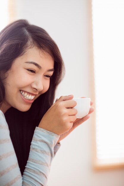 Mujer asiática que se relaja en el sofá con café