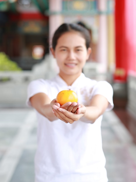 Mujer asiática que sostiene la naranja sagrada en el templo chino en Bangkok, Tailandia