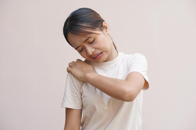 Mujer asiática que sufre de dolor en el hombro por estar sentada durante mucho tiempo en el trabajo