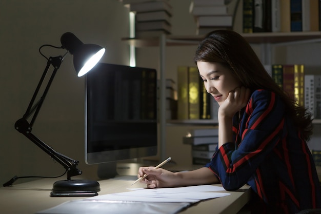 Mujer asiática que trabaja en casa por la noche usando la computadora para buscar información en línea.