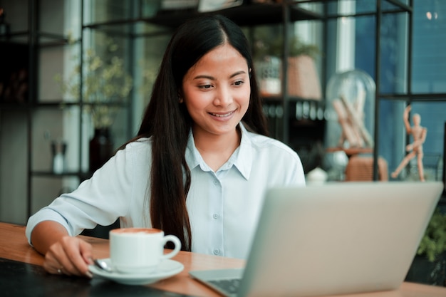 Mujer asiática que trabaja con la computadora portátil en la cafetería cafe