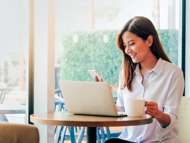 Mujer asiática que trabaja con la computadora portátil en cafetería.