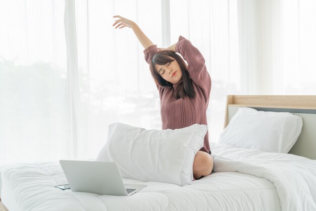 Mujer asiática que trabaja con la computadora portátil en cama