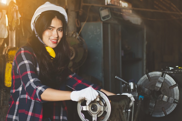 Mujer asiática que trabaja en la fábrica, industria que usa la máquina con feliz.