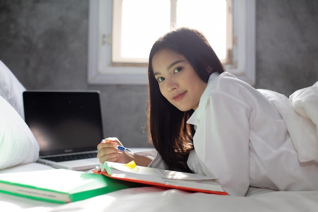 Mujer asiática que trabaja en línea desde casa con una computadora portátil en su cama para un nuevo estilo de vida normal