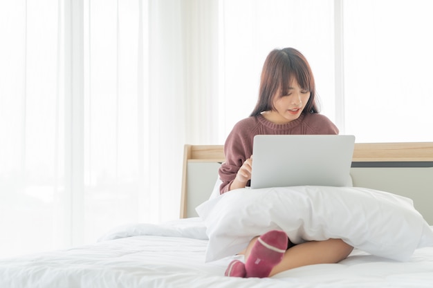 Mujer asiática que trabaja con el portátil en la cama