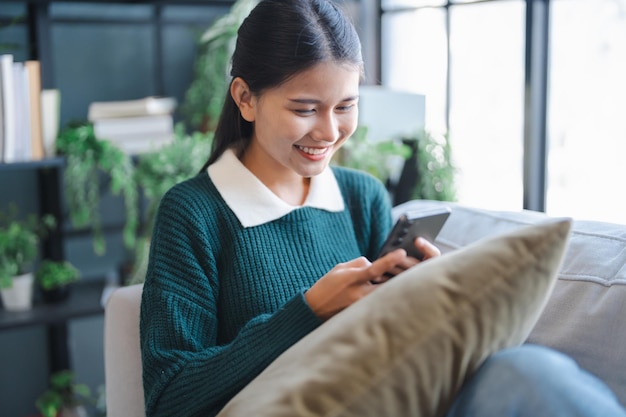Mujer asiática que usa asistente de voz en su teléfono inteligente en casa conversación con asistente en línea Bot de chat de voz conversacional AI Tecnologías modernas