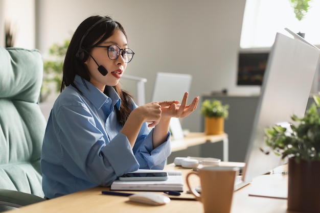 Mujer asiática que usa una computadora portátil con auriculares para hacer una videollamada