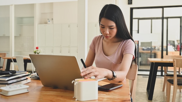 Mujer asiática que usa la computadora portátil en la tabla.