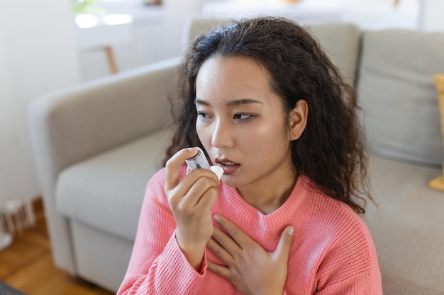 Mujer asiática que usa un inhalador mientras sufre de asma en casa Mujer joven que usa un inhalador para el asma Primer plano de una mujer asiática joven que usa un inhalador para el asma en casa