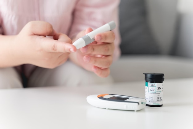 Mujer asiática que usa lanceta en el dedo para controlar el nivel de azúcar en la sangre con el medidor de glucosa diabetes glucemia