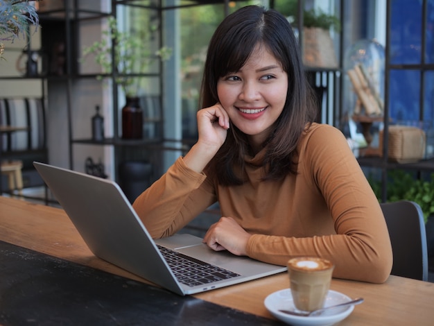 Mujer asiática que usa el ordenador portátil en café de la cafetería