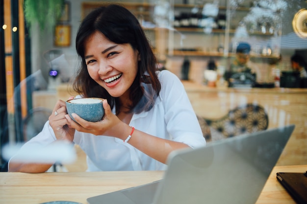 Mujer asiática que usa el ordenador portátil en café de la cafetería