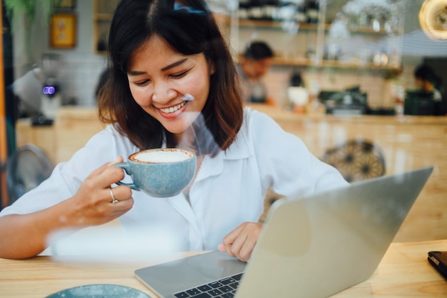 Mujer asiática que usa el ordenador portátil en café de la cafetería