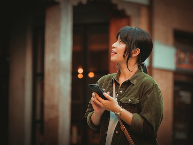 Mujer asiática que usa smartphone con humor feliz en alameda de compras