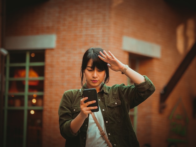 Mujer asiática que usa smartphone con humor feliz en alameda de compras