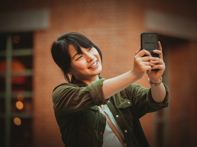 Mujer asiática que usa smartphone con humor feliz en alameda de compras