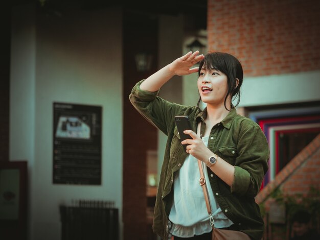 Mujer asiática que usa smartphone con humor feliz en alameda de compras