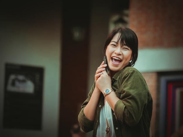 Mujer asiática que usa smartphone con humor feliz en alameda de compras