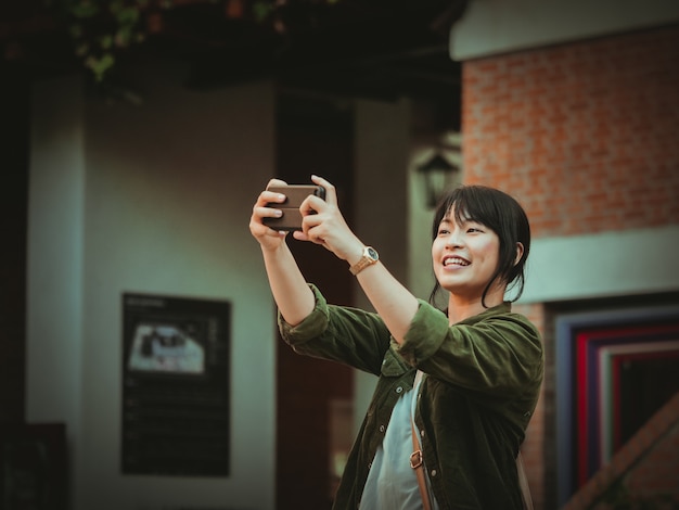 Mujer asiática que usa smartphone con humor feliz en alameda de compras