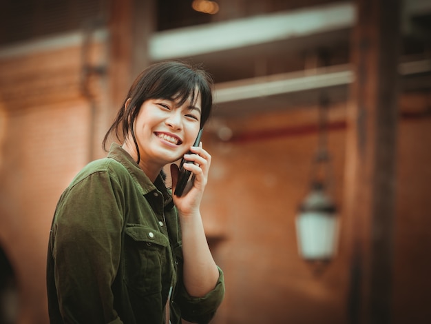 Mujer asiática que usa smartphone con humor feliz en alameda de compras