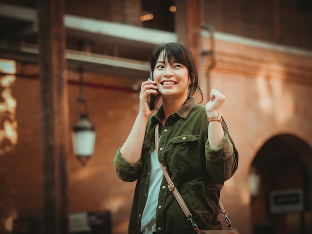 Mujer asiática que usa smartphone con humor feliz en alameda de compras