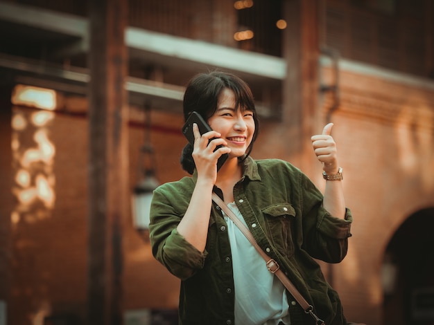 Mujer asiática que usa smartphone con humor feliz en alameda de compras