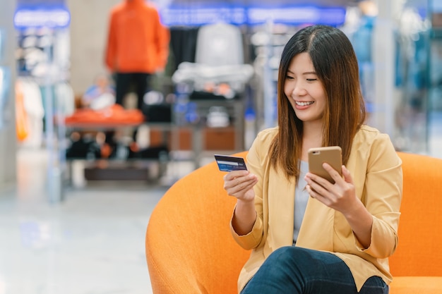 Mujer asiática que usa tarjeta de crédito con el teléfono móvil para compras en línea en grandes almacenes