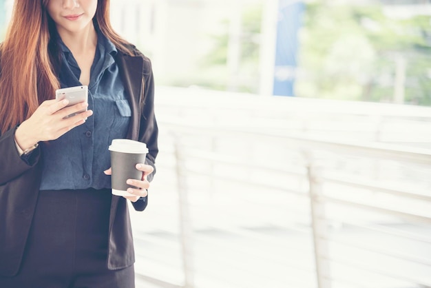 Mujer asiática que usa el teléfono celular caminando por la calle de la ciudad Teléfono inteligente mujer segura de sí misma ciudad moderna