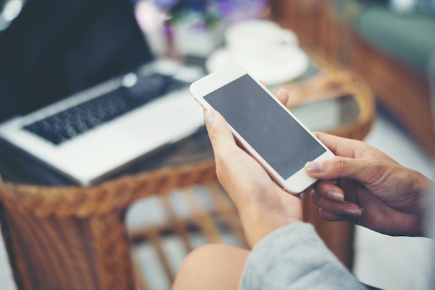 Mujer asiática que usa el teléfono elegante en café que bebe el café.