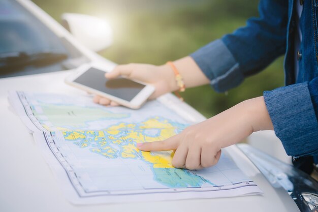 Mujer asiática que usa un teléfono inteligente y un mapa entre conducir un auto en un viaje por carretera