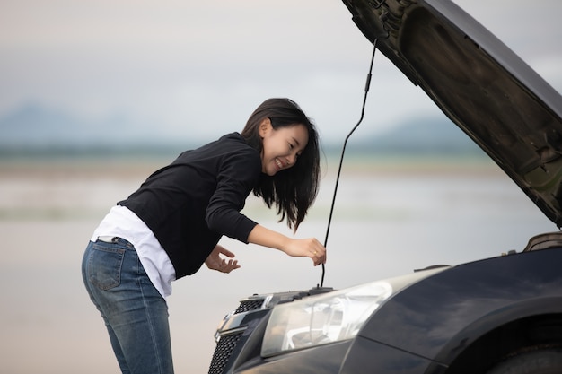 Mujer asiática que usa el teléfono móvil mientras que mira y tensionado Hombre que se sienta después de la avería del coche