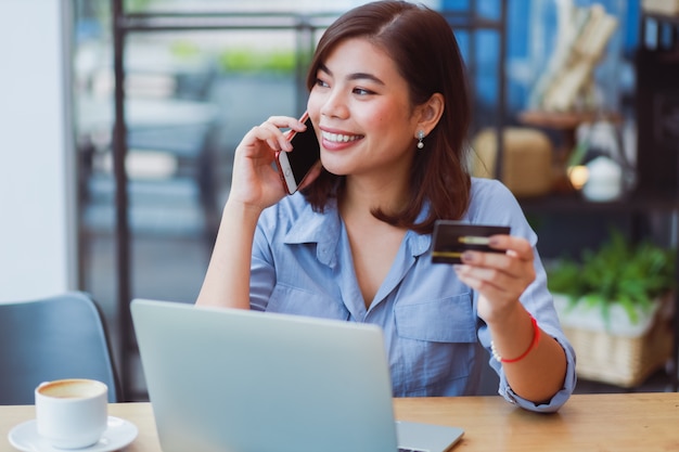 Mujer asiática que usa el teléfono móvil con tarjeta de crédito y computadora portátil para comprar pagos en línea en la cafetería cafetería con amigos