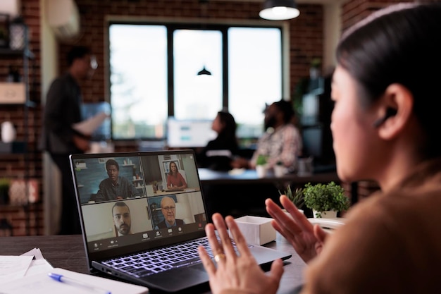 Foto mujer asiática que usa el teletrabajo de videollamadas para chatear con personas en una computadora portátil, hablando en una reunión de videoconferencia remota. conversación en internet de cámara web en teleconferencia en línea con auriculares.