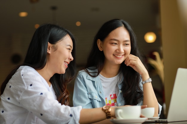 Mujer asiática que usa el trabajo del ordenador portátil y café de la bebida en café