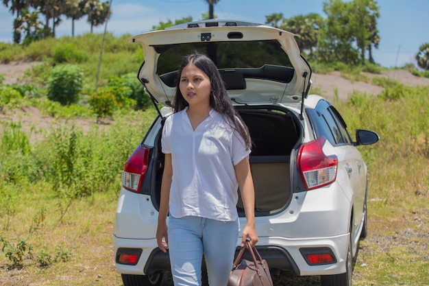 Mujer asiática que va de vacaciones cargando el maletero de su coche con maletas de viaje