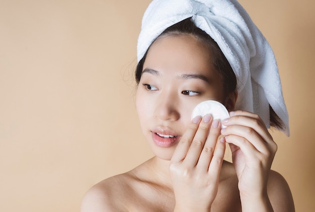 Mujer asiática quita el maquillaje, con una toalla en la cabeza.