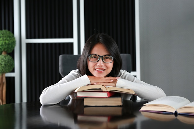 La mujer asiática se relaja y sonríe en el libro en la biblioteca.