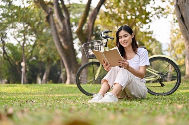 Mujer asiática relajada leyendo un libro sobre la hierba en el concepto de estilo de vida del parque público