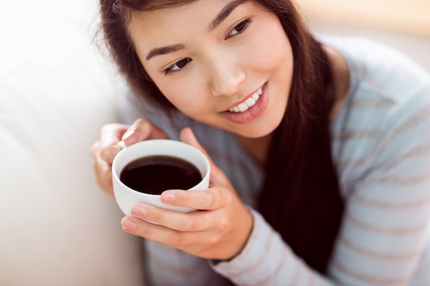 Mujer asiática relajante en el sofá con café