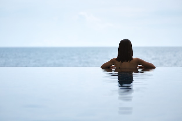 Mujer asiática relajarse en la piscina en la playa