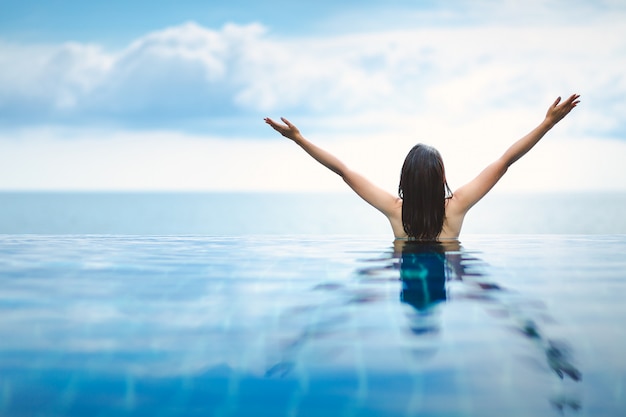 Mujer asiática relajarse en la piscina en la playa