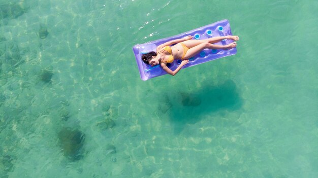 Mujer asiática relajarse tomando el sol en el sofá de aire en el hermoso mar verde