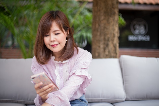 Foto mujer asiática del retrato que usa un teléfono elegante en jardín de la cafetería