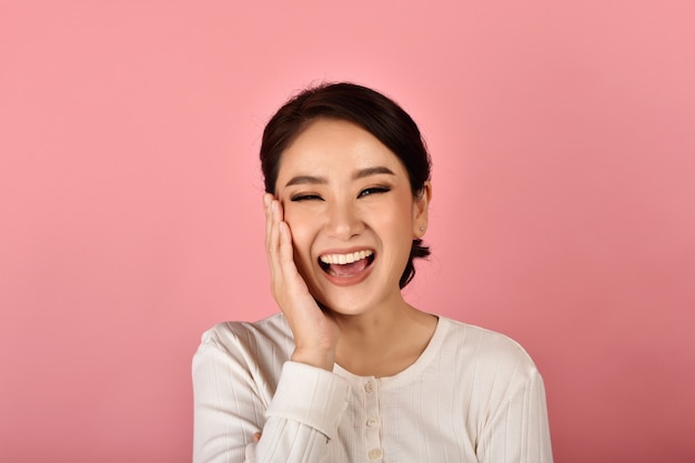 Mujer asiática riendo y disfruta en pared rosa