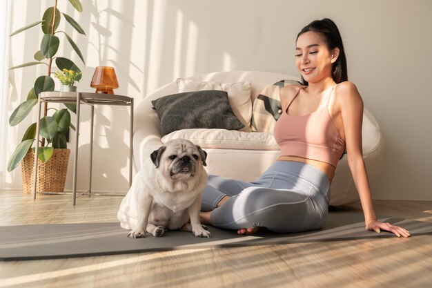 Mujer asiática en ropa deportiva haciendo ejercicio y haciendo yoga con un lindo perro en la sala de estar de casa