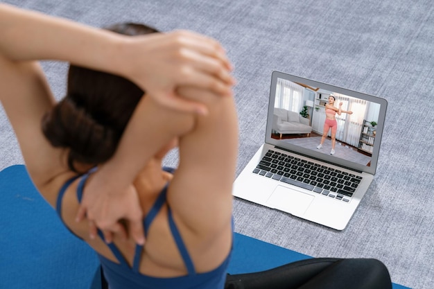 Foto mujer asiática en ropa deportiva haciendo ejercicio de yoga en una colchoneta de fitness como su rutina de entrenamiento en casa mujer de estilo de vida de cuidado corporal saludable viendo videos de yoga en línea en una computadora portátil vigoroso