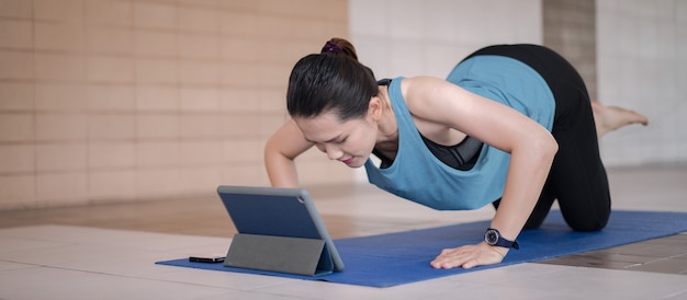 Mujer asiática en ropa deportiva que se ejercita después del programa de entrenamiento en línea a través de una tableta digital en casa