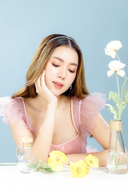 Una mujer asiática con un rostro hermoso y una piel fresca y suave está vestida de rosa. Modelo de mujer linda con maquillaje natural y ojos brillantes está posando y mirando a la cámara sobre fondo azul aislado.