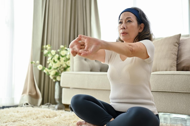 Mujer asiática saludable estirando las manos practicando yoga en la sala de estar de su casa